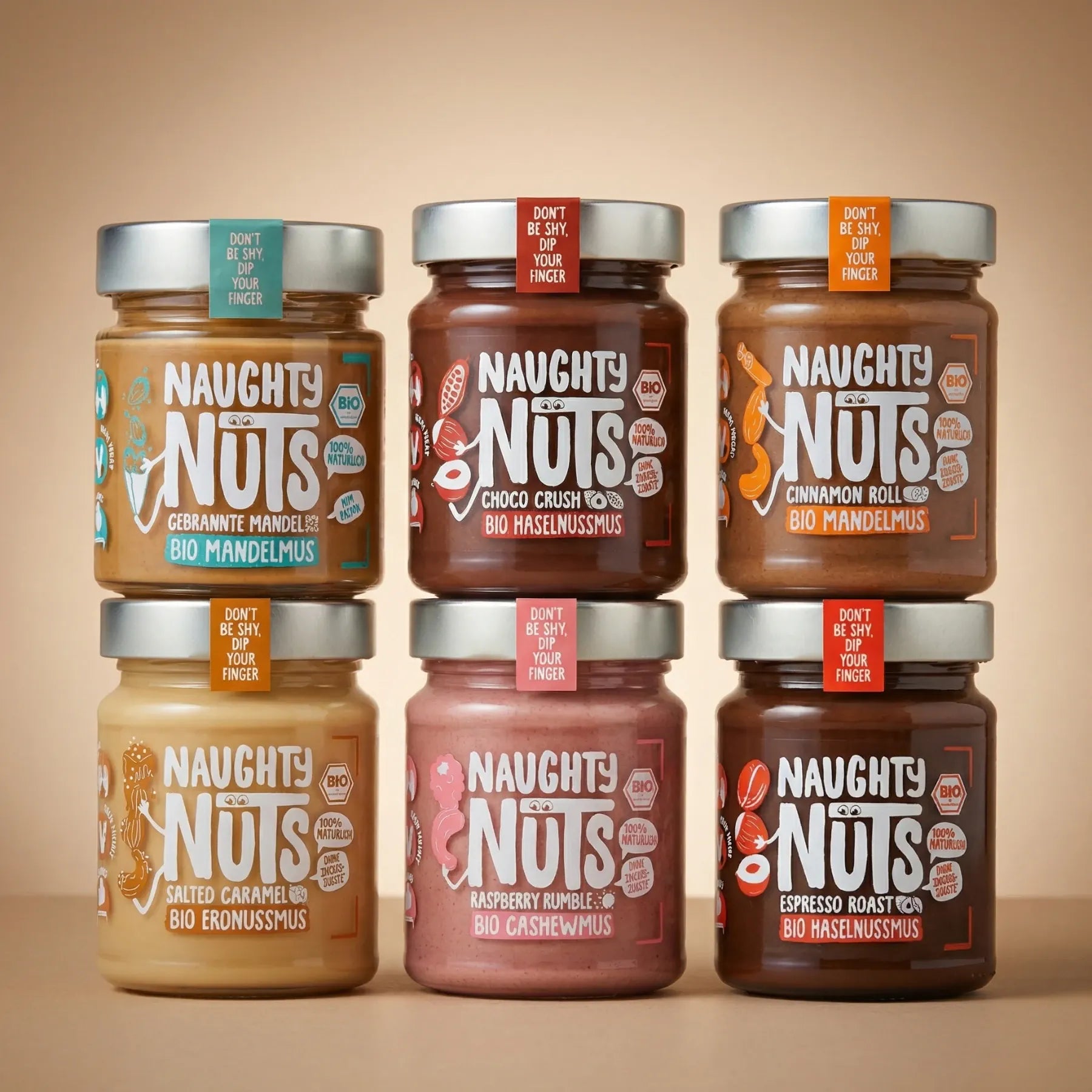 Sechs Gläser Naughty Nuts Nussmus in verschiedenen Geschmacksrichtungen, gestapelt in zwei Reihen